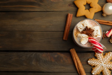 Flat lay composition with glass cup of tasty cocoa and Christmas candy cane on wooden table. Space for text