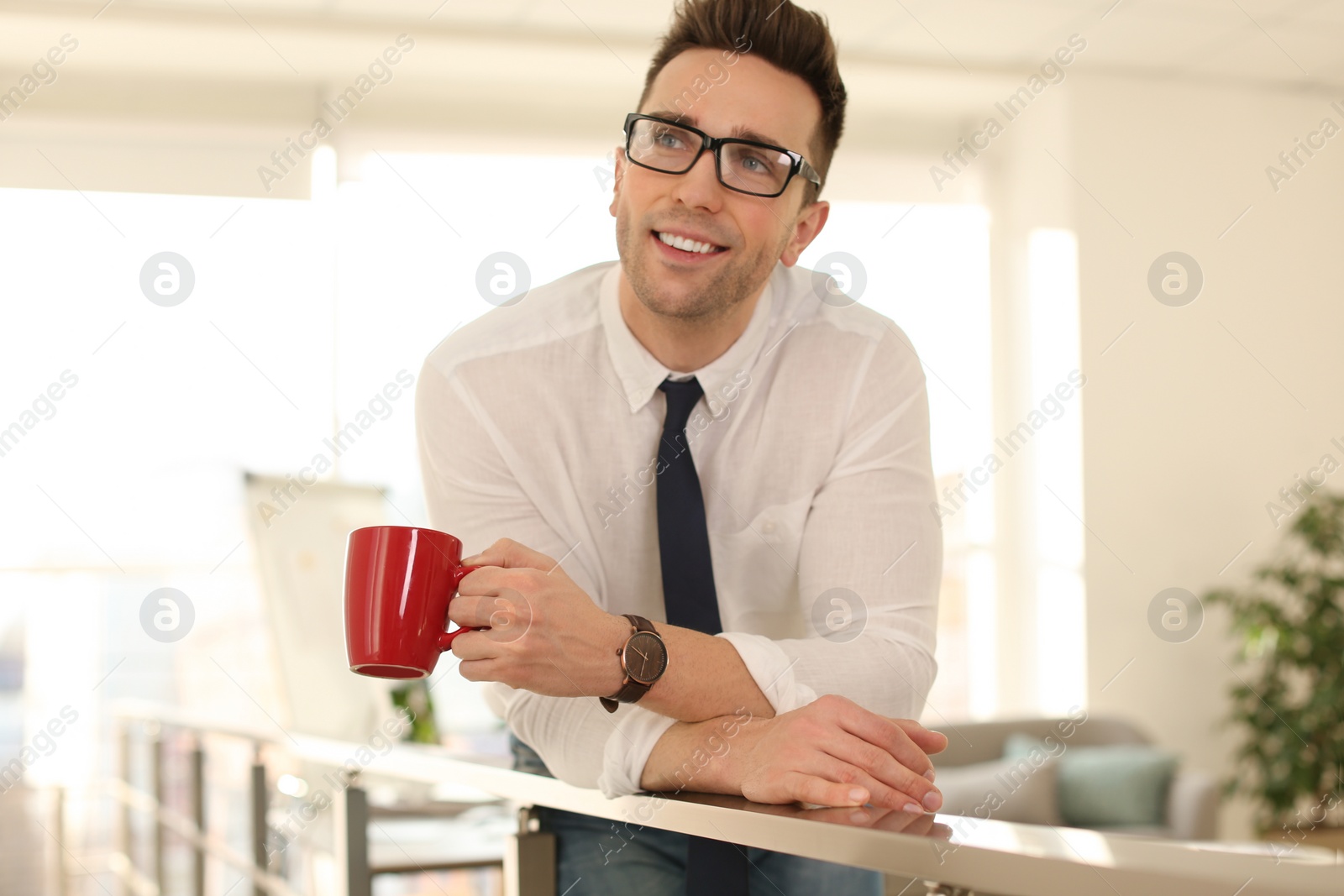 Photo of Young businessman with cup of drink relaxing in office during break