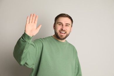 Photo of Happy young man waving to say hello on light grey background