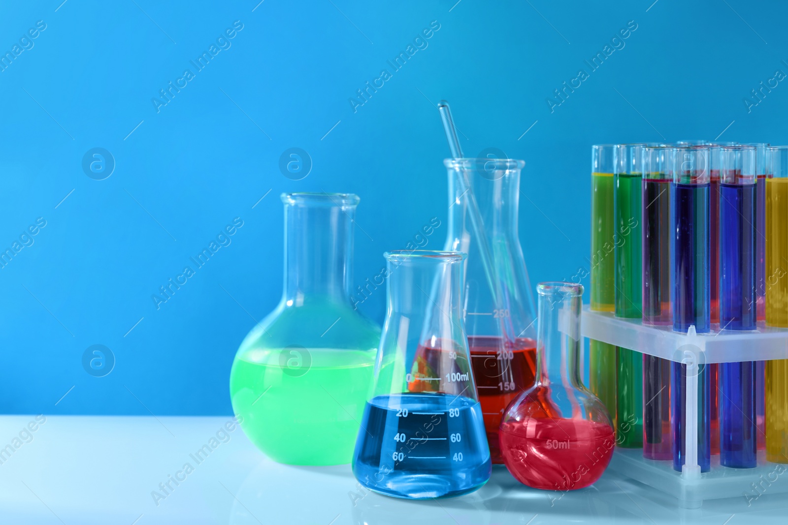 Photo of Different laboratory glassware with colorful liquids on white table against light blue background