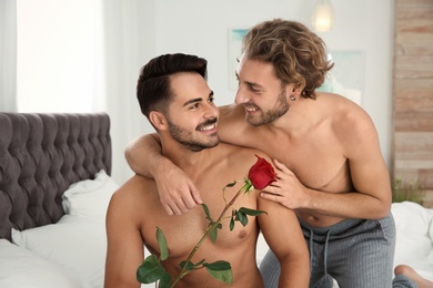 Photo of Happy gay couple with flower on bed at home