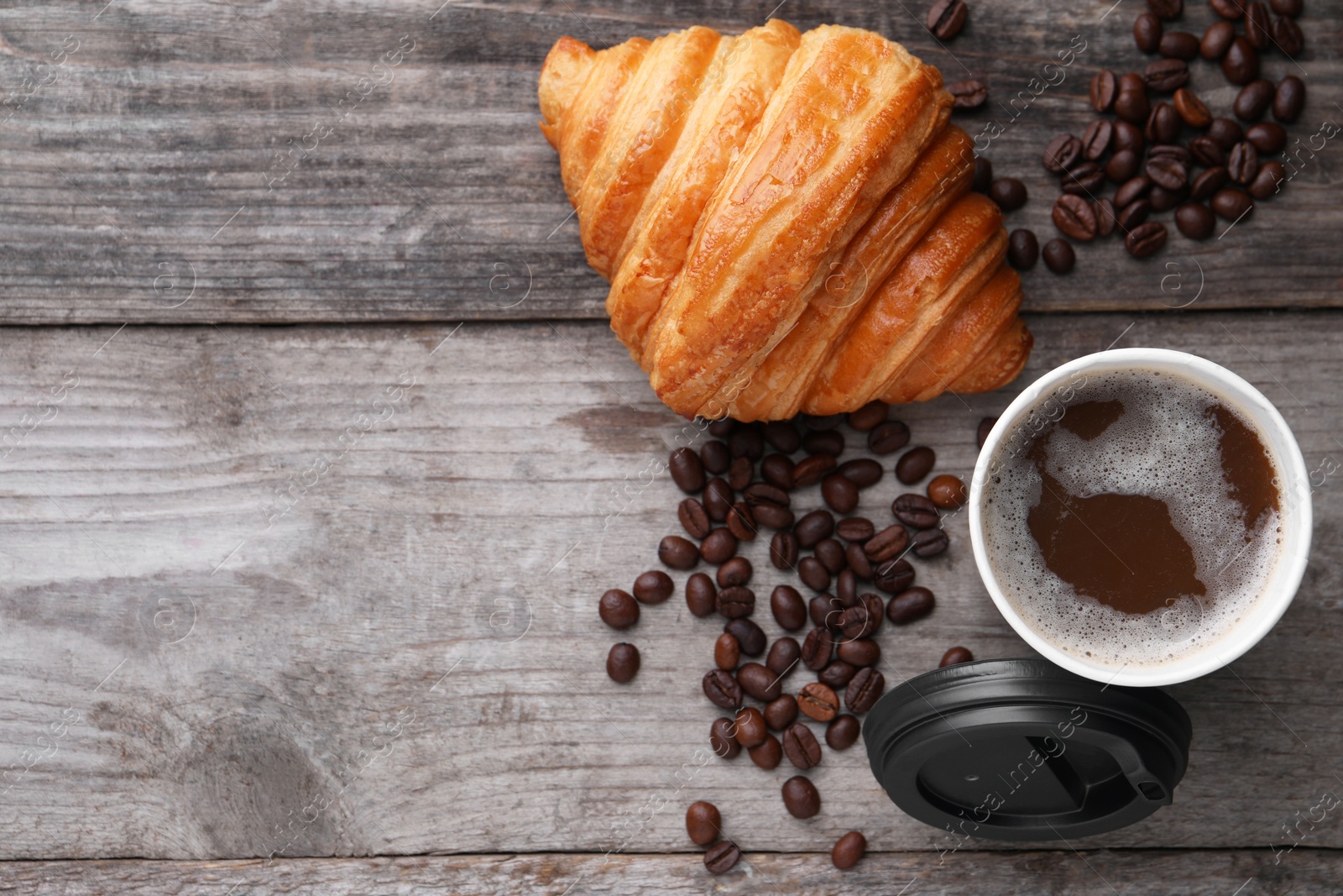 Photo of Coffee to go. Paper cup of tasty drink, croissant and beans on wooden table, flat lay with space for text