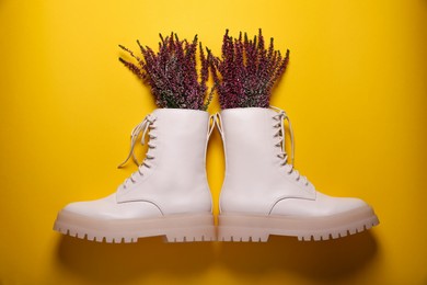 Photo of Pair of stylish leather shoes with heather flowers on yellow background, flat lay