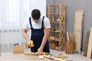 Photo of Young worker using electric drill at table in workshop