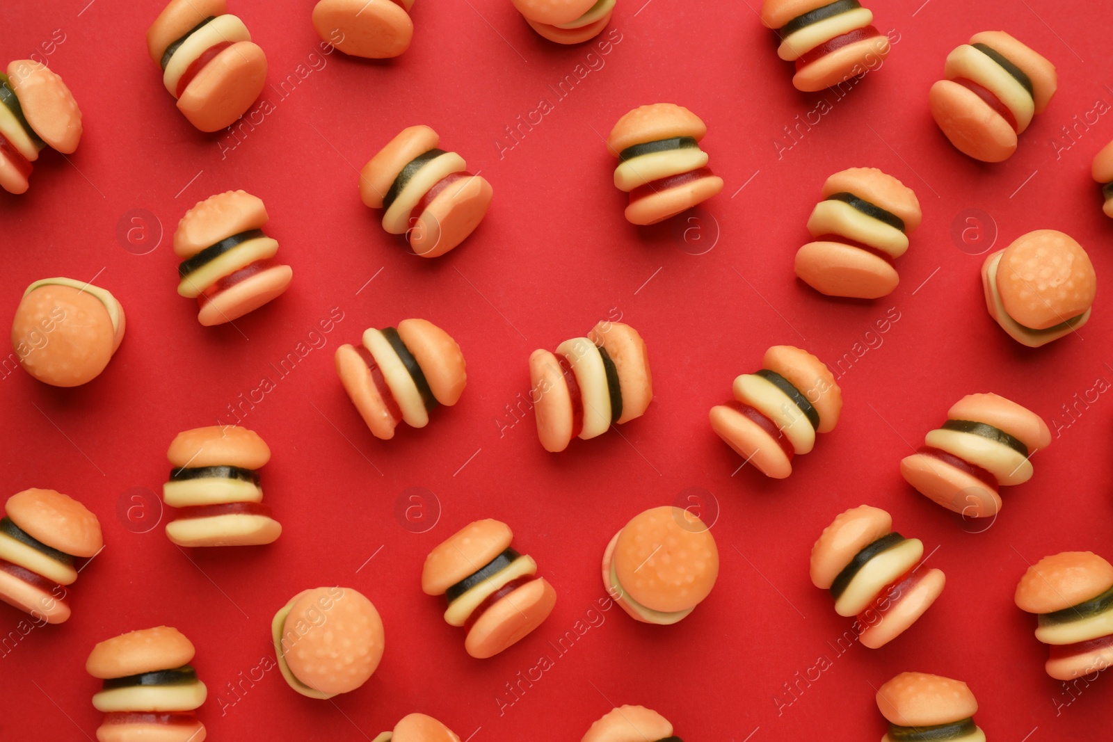 Photo of Tasty jelly candies in shape of burger on red background, flat lay