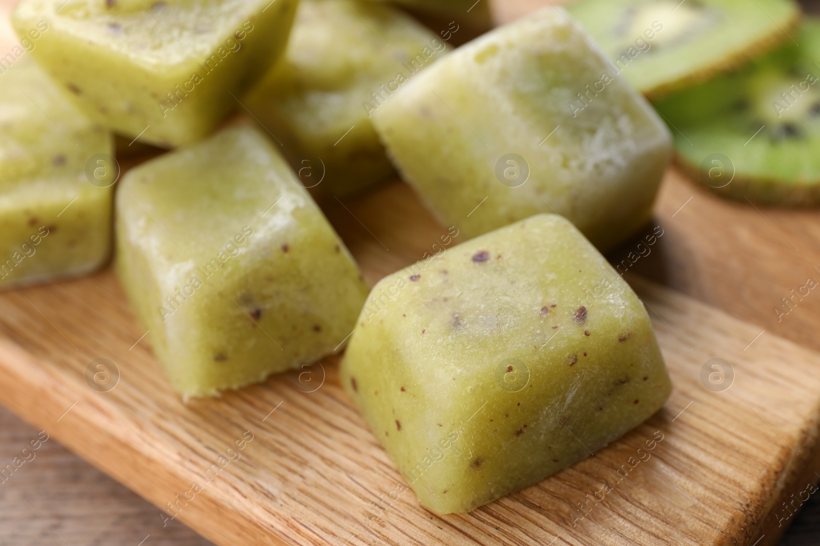 Photo of Frozen kiwi puree cubes and ingredient on wooden board, closeup