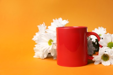 Photo of One red ceramic mug and beautiful flowers on orange background