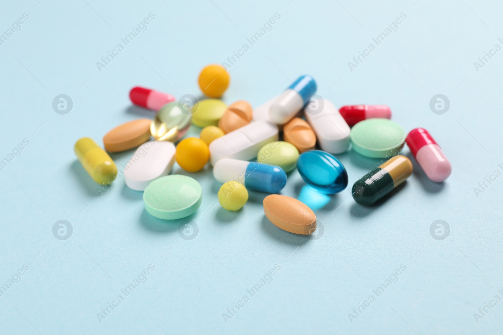 Photo of Many different pills on light blue background, closeup