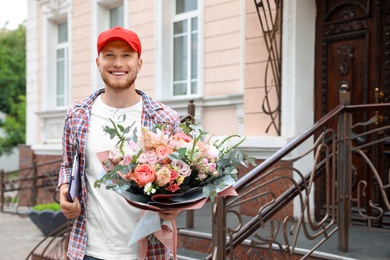 Happy delivery man with beautiful flower bouquet outdoors