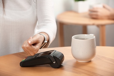 Woman using terminal for contactless payment with smart watch in cafe