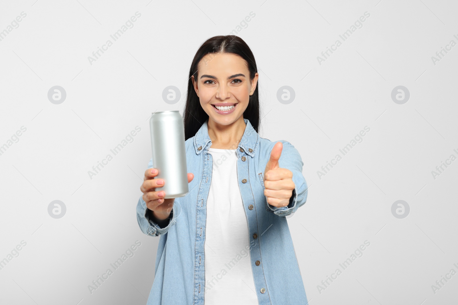 Photo of Beautiful happy woman holding beverage can and showing thumbs up on light grey background