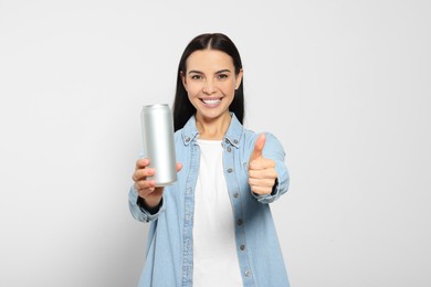 Photo of Beautiful happy woman holding beverage can and showing thumbs up on light grey background