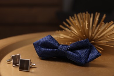 Photo of Stylish blue bow tie and cufflinks on golden table, closeup