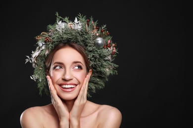 Photo of Beautiful young woman wearing Christmas wreath on black background. Space for text