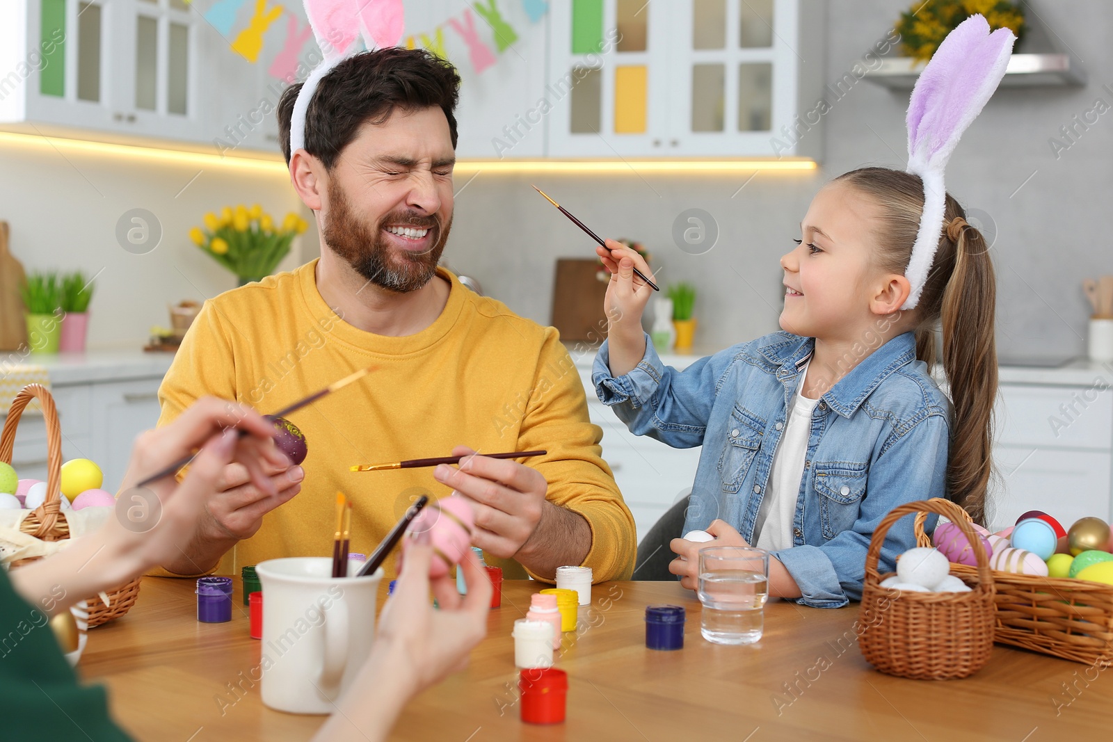 Photo of Happy family having fun while painting Easter eggs at table in kitchen