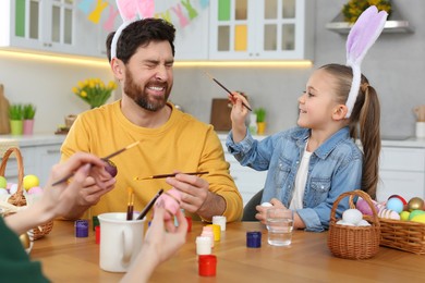 Photo of Happy family having fun while painting Easter eggs at table in kitchen