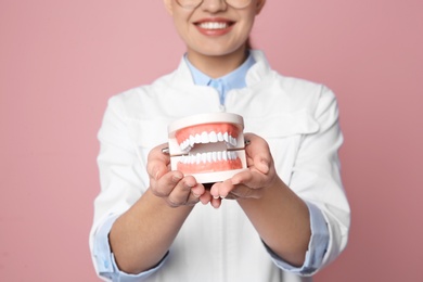 Photo of Female dentist holding jaws model on color background, closeup