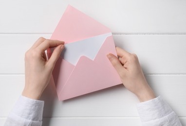 Woman taking card out of letter envelope at white wooden table, top view