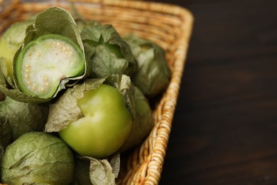 Photo of Fresh green tomatillos with husk in wicker basket on table, closeup