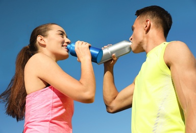 Photo of Young sporty couple drinking from water bottles against blue sky on sunny day