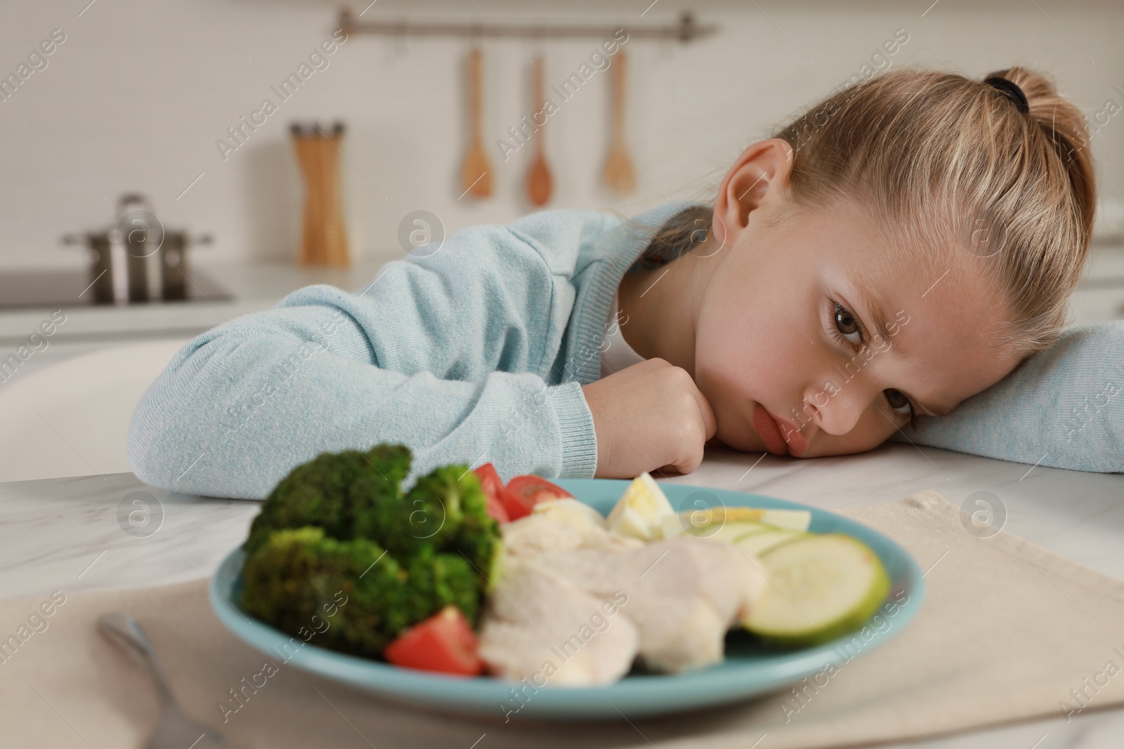 Photo of Cute little girl refusing to eat dinner in kitchen