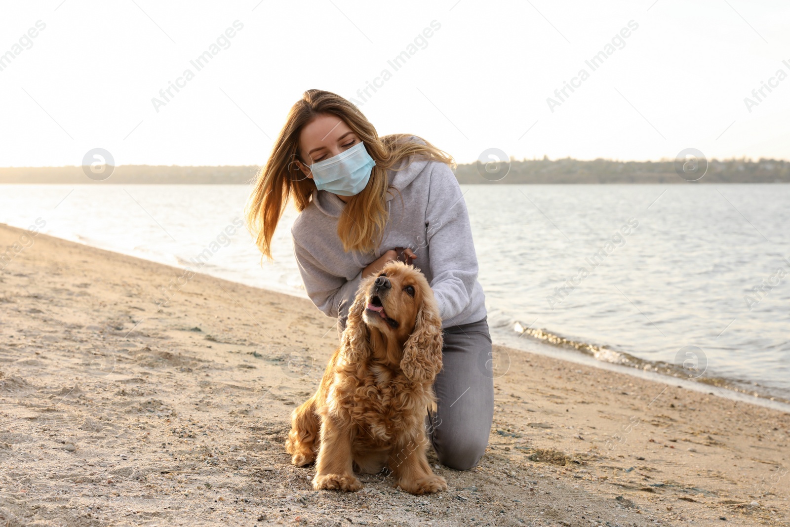 Photo of Woman in protective mask with English Cocker Spaniel on beach. Walking dog during COVID-19 pandemic