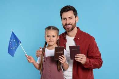 Immigration. Happy man with his daughter holding passports and flag of European Union on light blue background