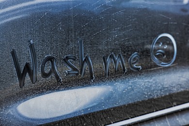 Phrase Wash Me and sad emoticon drawn on dirty car, closeup