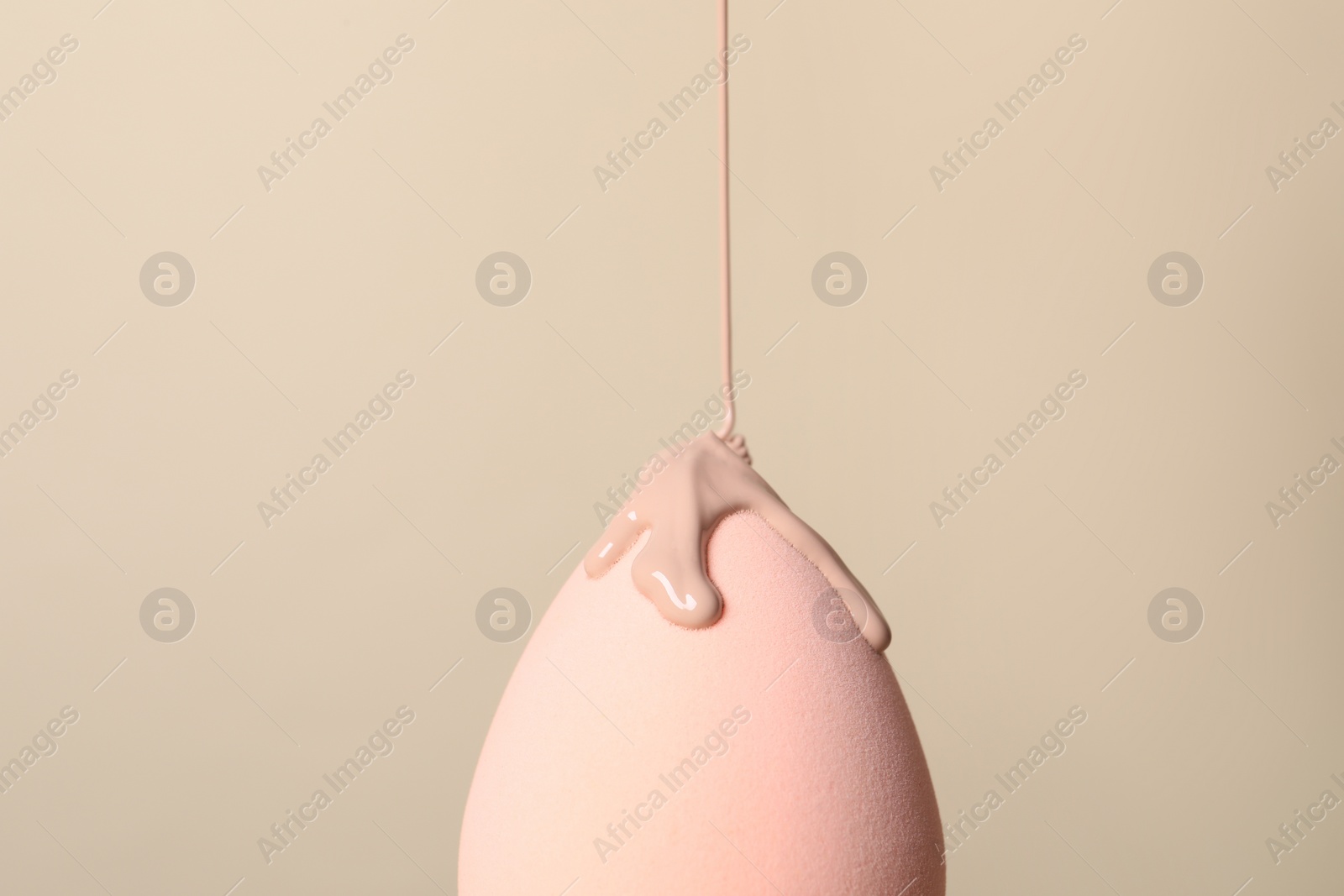 Photo of Skin foundation pouring onto makeup sponge on beige background