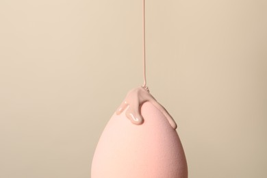 Photo of Skin foundation pouring onto makeup sponge on beige background