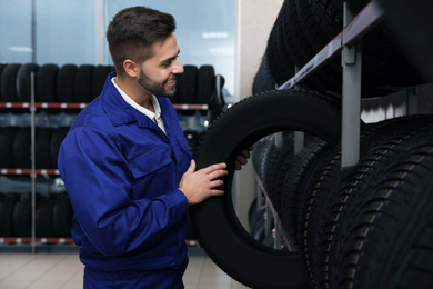 Male mechanic with car tire in auto store