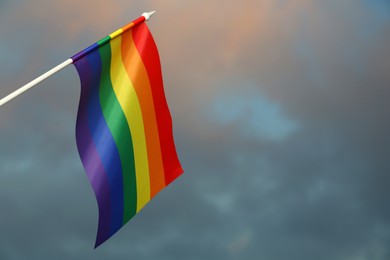 Photo of Bright rainbow LGBT flag against cloudy sky, space for text