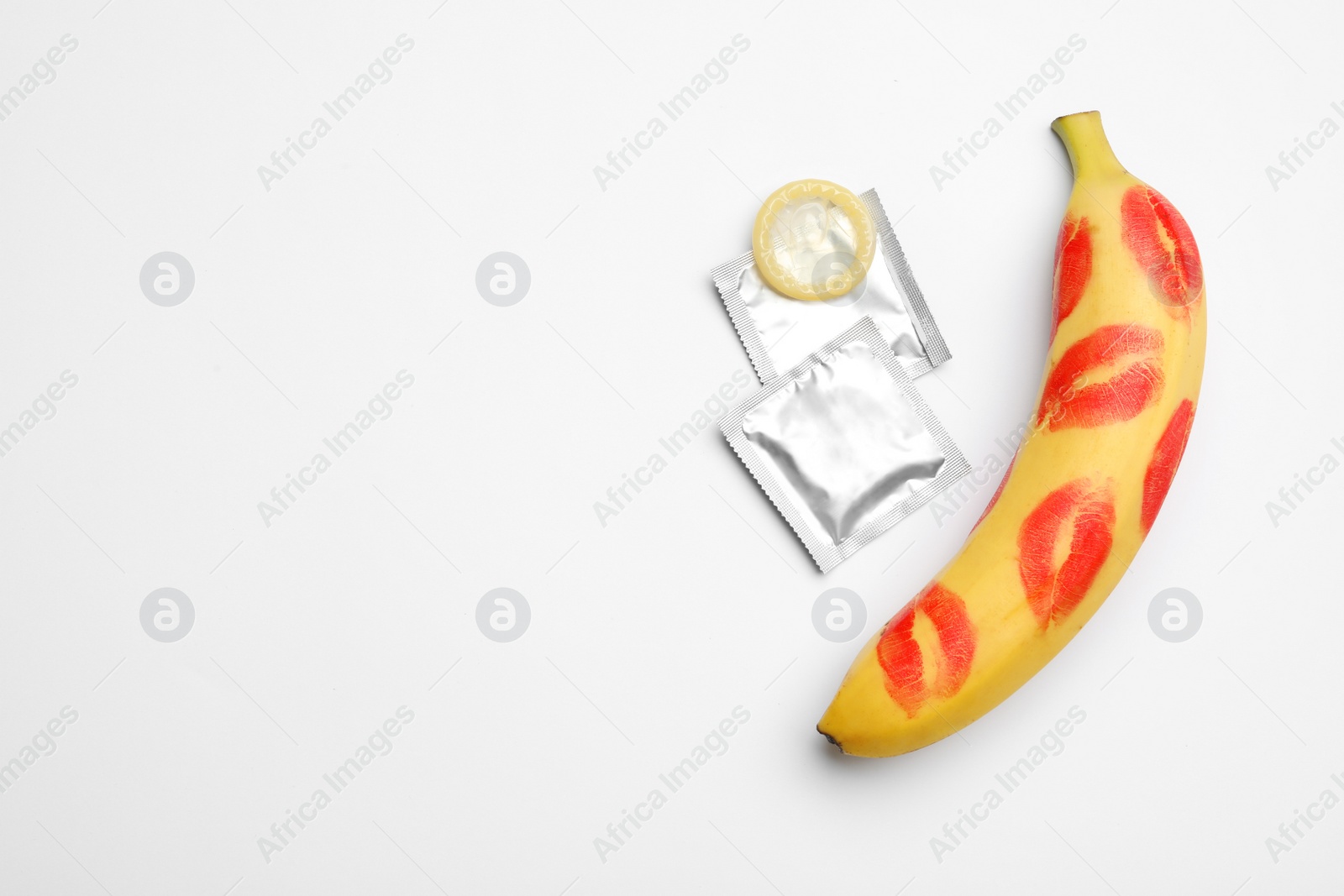 Photo of Condoms and banana with lipstick kiss marks on white background, top view. Safe sex