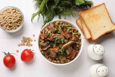 Delicious lentils with mushrooms, bacon and green onion in bowl served on white table, flat lay
