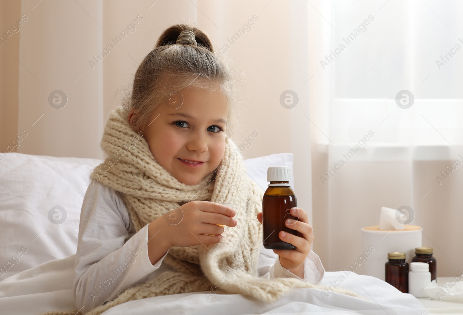Photo of Sick girl taking cough syrup on bed at home, space for text. Cold medicine