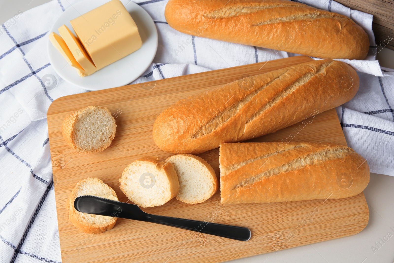 Photo of Tasty cut baguette with fresh butter on white table