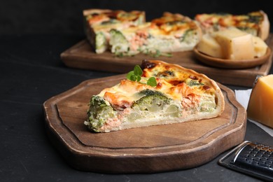 Photo of Piece of delicious homemade quiche with salmon and broccoli on black table