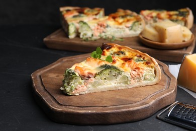 Piece of delicious homemade quiche with salmon and broccoli on black table