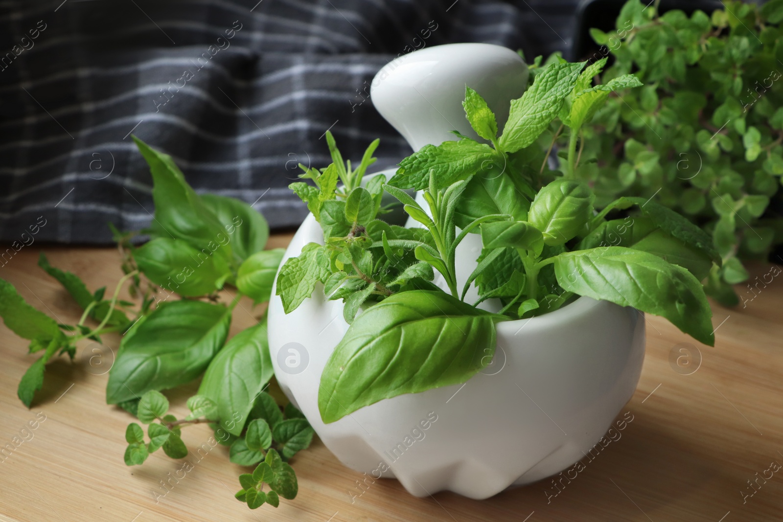 Photo of Mortar with different fresh herbs on wooden table, closeup