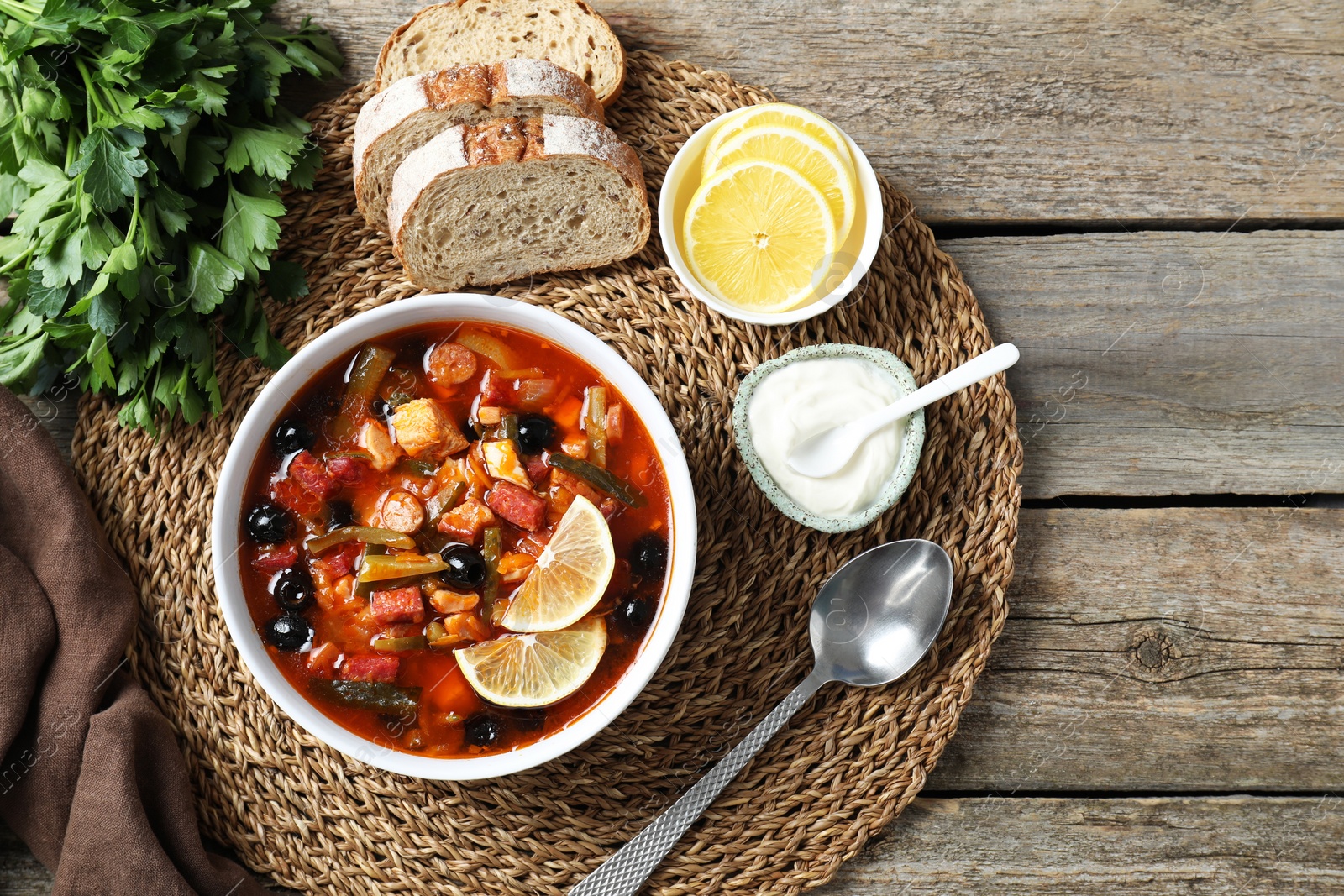 Photo of Meat solyanka soup with sausages, olives and vegetables served on wooden table, flat lay. Space for text