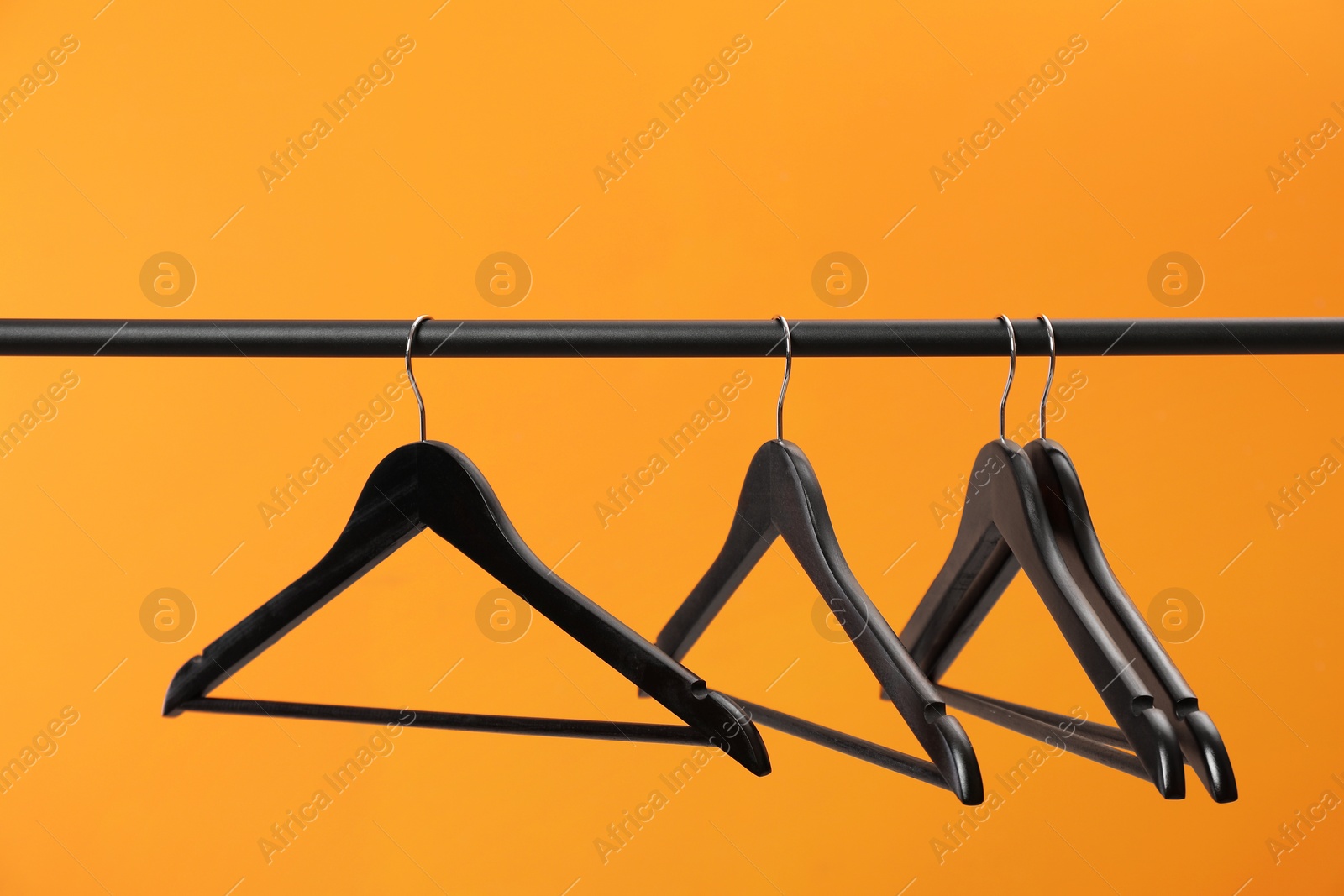 Photo of Black clothes hangers on rack against orange background