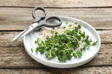 Plate with cut fresh radish microgreens and scissors on wooden table