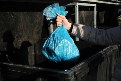 Photo of Woman throwing trash bag full of garbage in bin outdoors, closeup