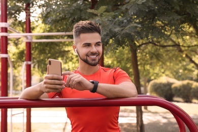 Young man with wireless headphones and mobile device listening to music on sports ground