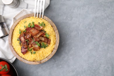 Photo of Cooked cornmeal with bacon and microgreens in bowl on light grey table, top view. Space for text