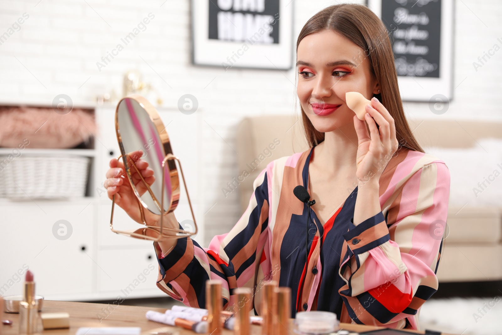 Photo of Young beauty blogger applying foundation at home