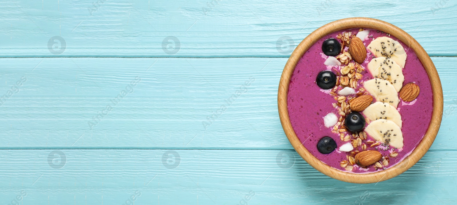 Photo of Delicious acai smoothie with granola and almonds in dessert bowl on light blue wooden table, top view. Space for text