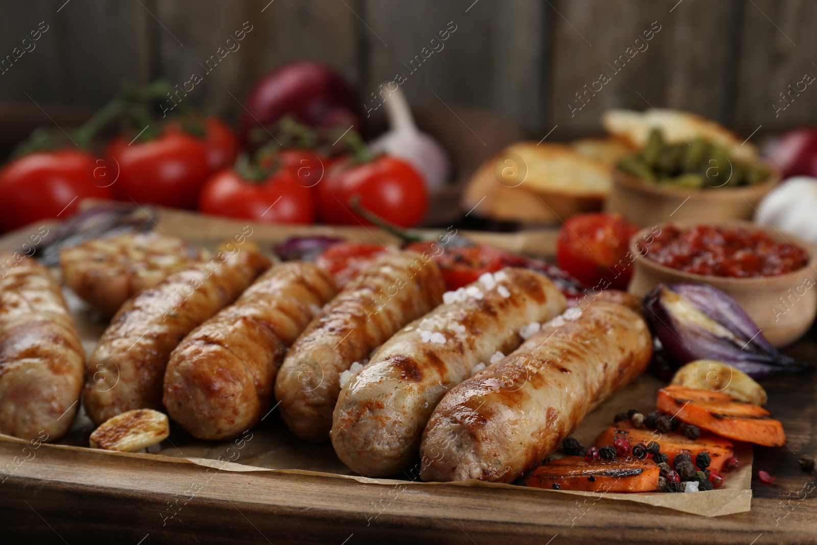 Photo of Tasty grilled sausages with vegetables on wooden board, closeup