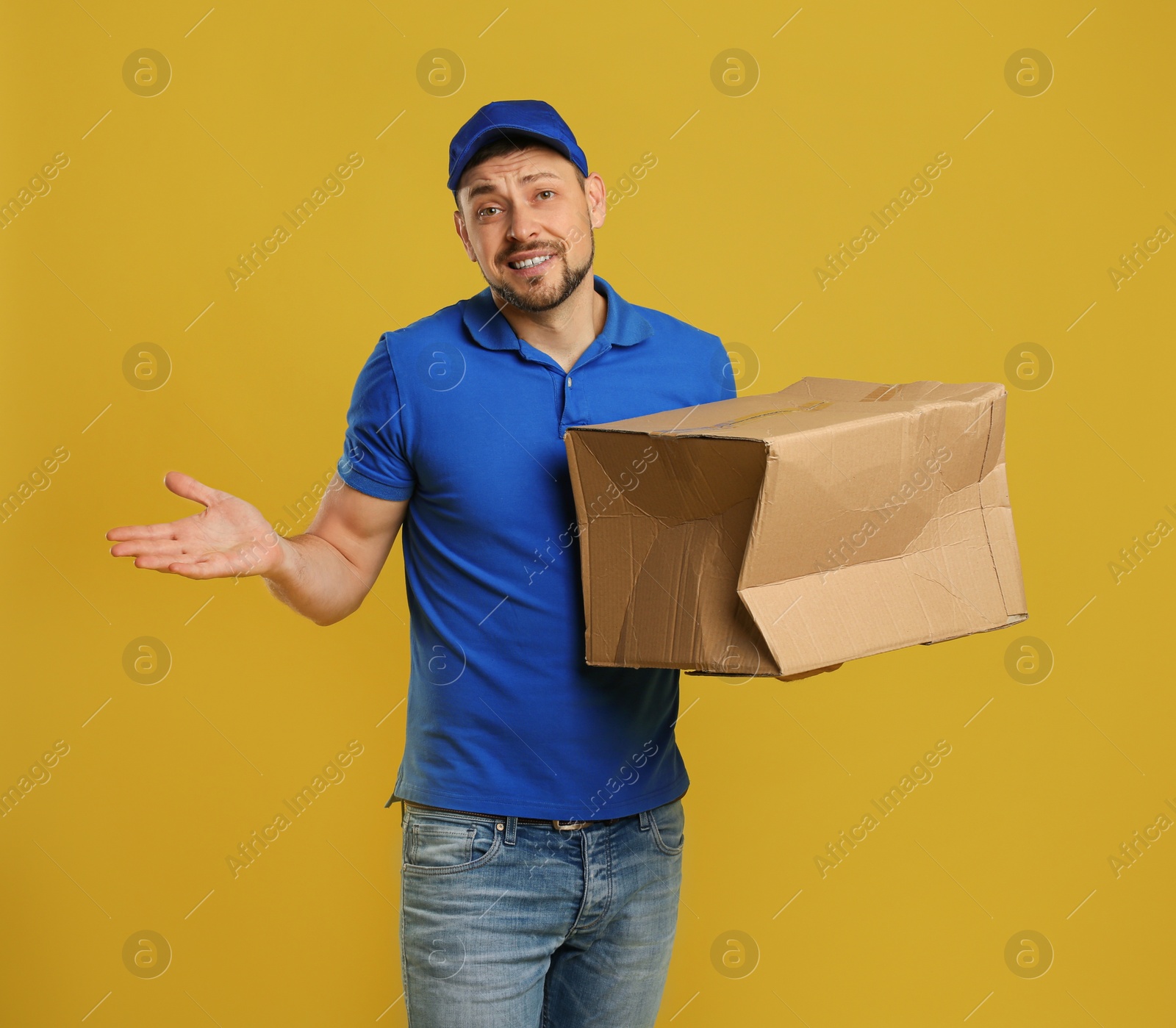 Photo of Emotional courier with damaged cardboard box on yellow background. Poor quality delivery service