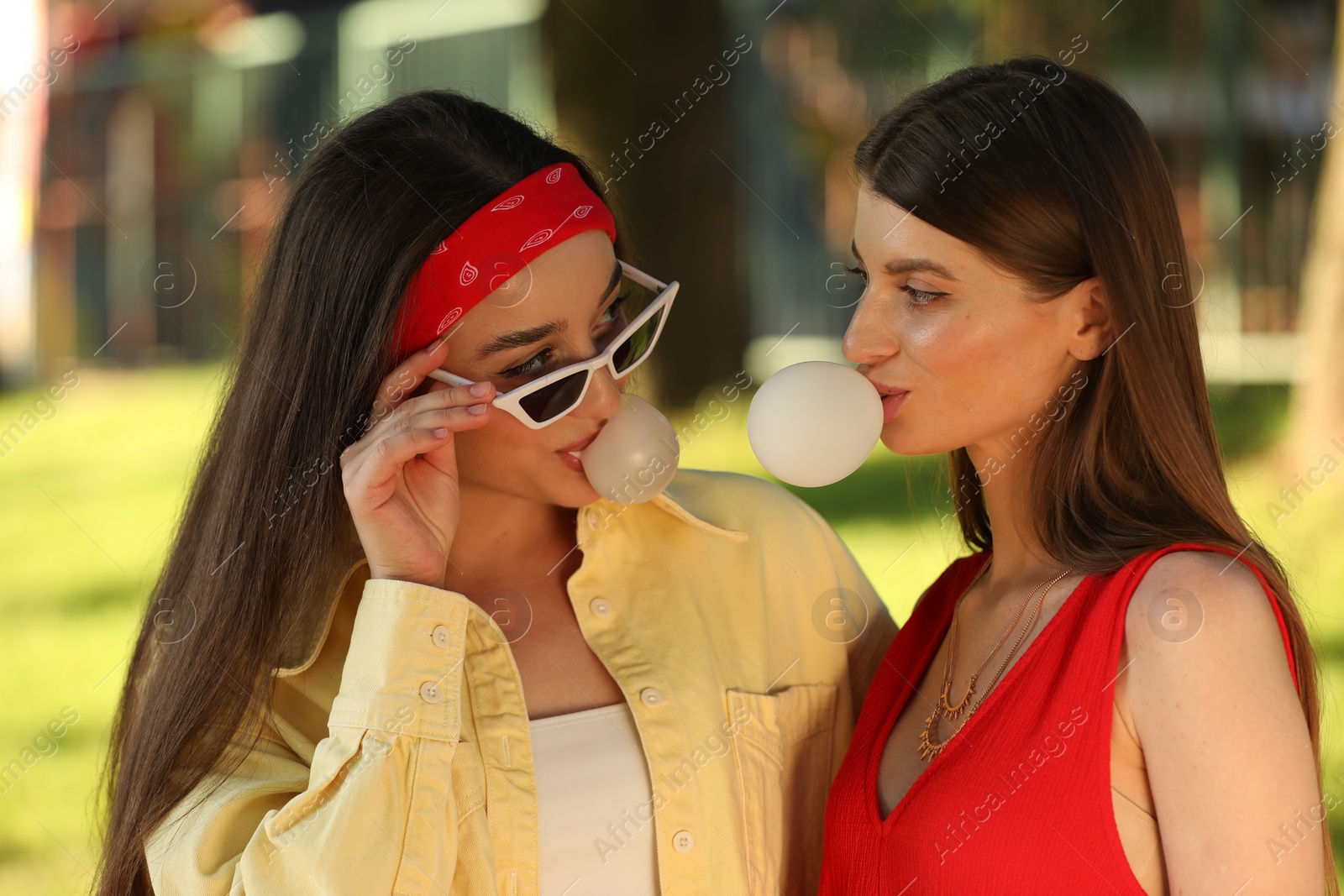 Photo of Beautiful young women blowing bubble gums in park